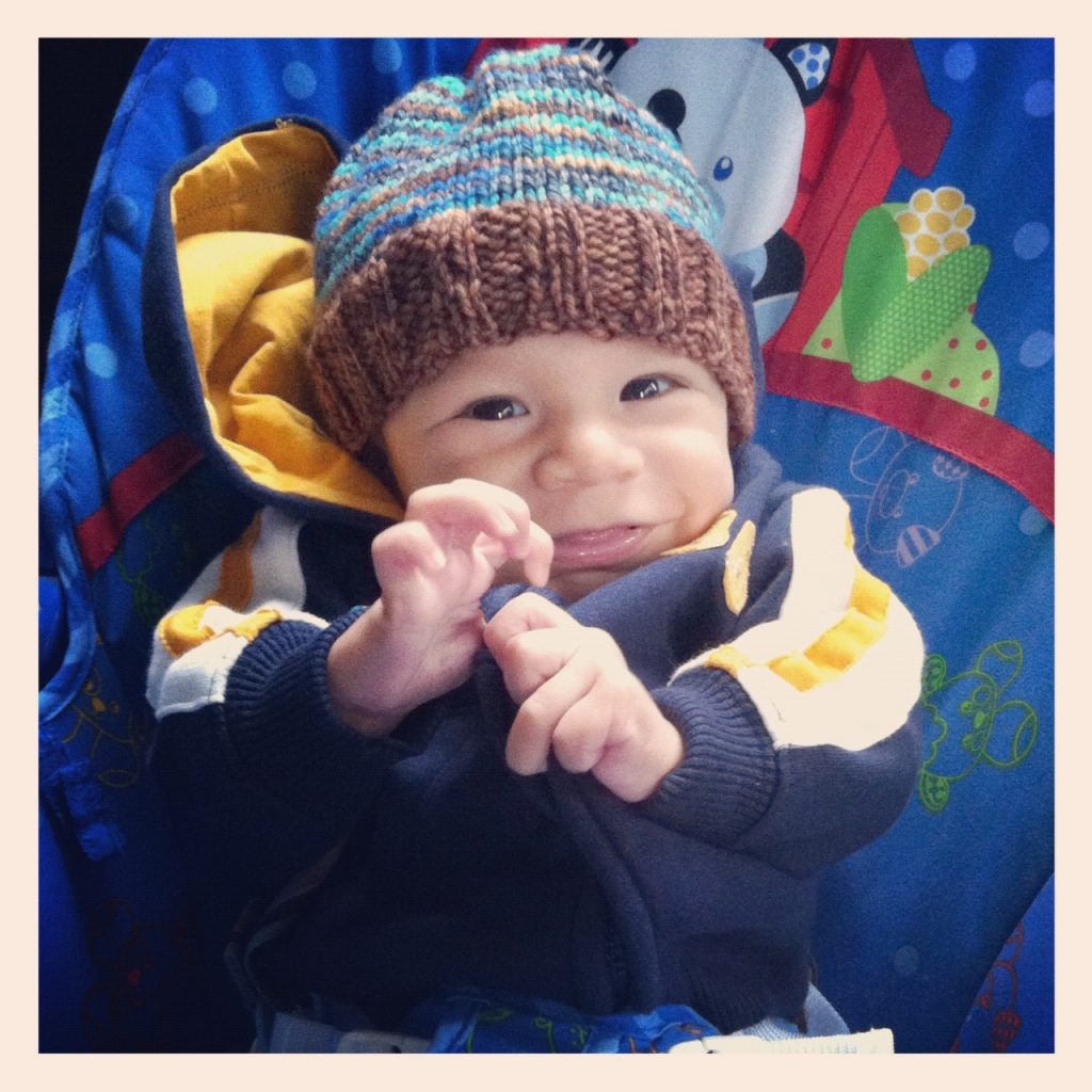 A beautiful smiling rainbow baby boy wearing a crocheted hat and a giant smile on his face. 