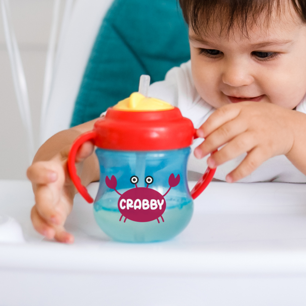 Baby holding a sippy cup with a crab that says crabby on its shell. 